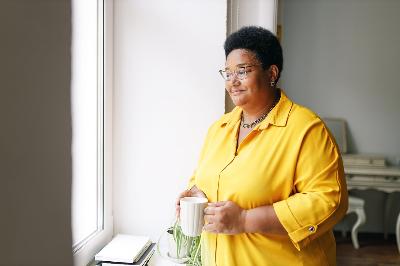 Smilng, older woman holding a coffe cup and looking out the window