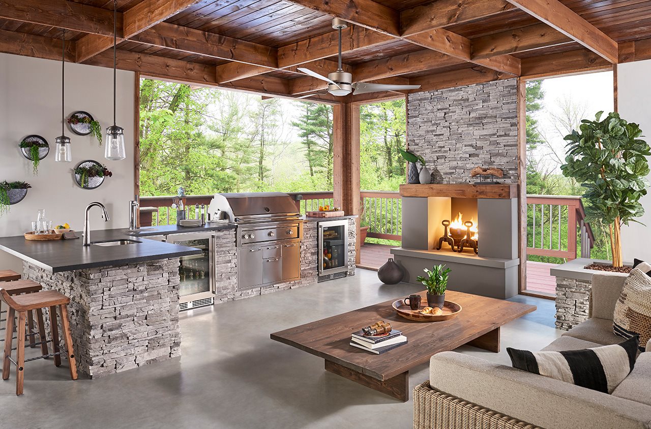 A grill and kitchen counter next to a fireplace on a well furnished outdoor space.