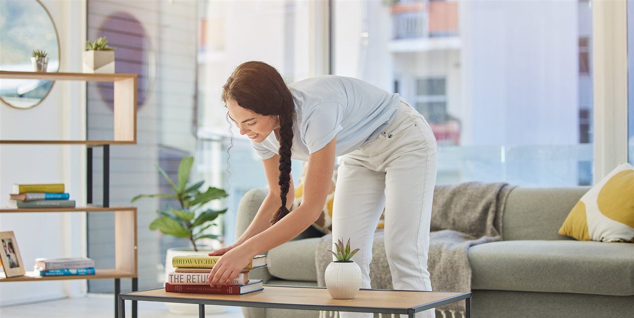 Woman moving a stack of books on a coffee table.