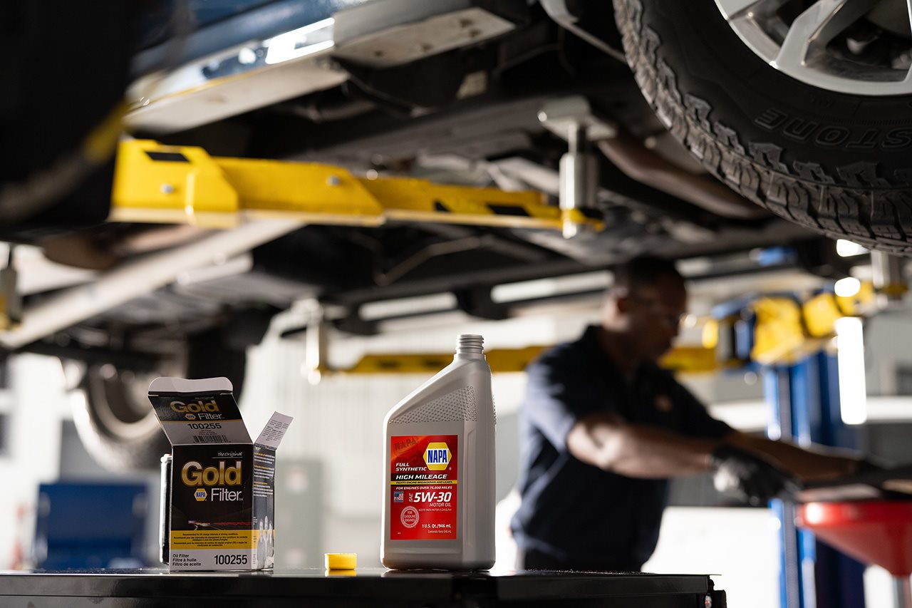 A NAPA Gold oil filter and bottle of NAPA SW-30 motor oil sit on a table under an elevated vehicle.