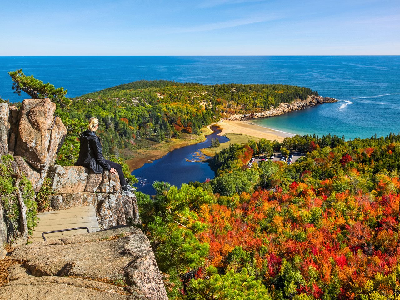 Woman sitting on a cliff enjoying the view of sand beach