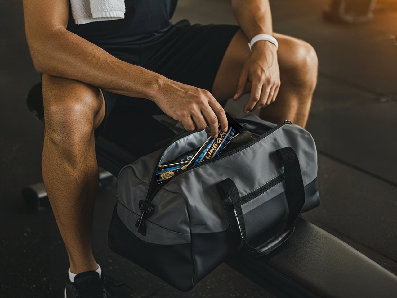 Man sitting on a bench in a locker room pulling a Linear bar out of his gym bag