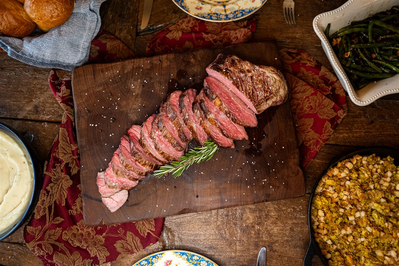 The Lickley Family's Slow-Roasted Tri-Tip carved on a wooden tray surrounded by side dishes on dinning room table.