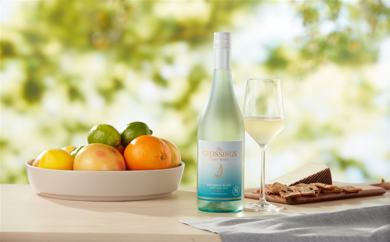 A bottle of the crossing wine on an outdoor table with a bowl of oranges and limes.