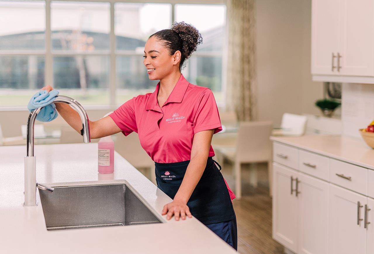 Molly maid cleaning the sink in the kitchen.