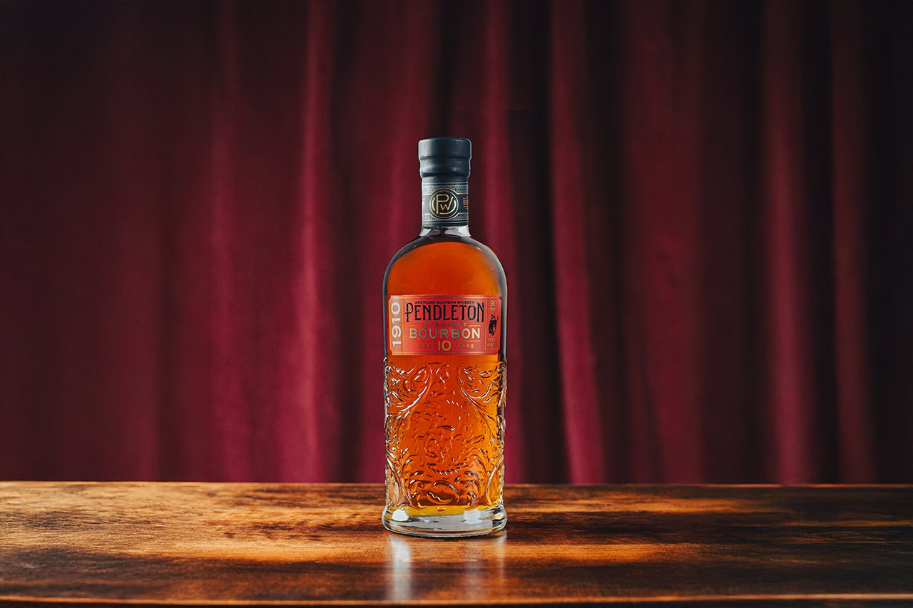 A bottle of Pendleton Whiskey sitting on a stage with a red curtain behind it.