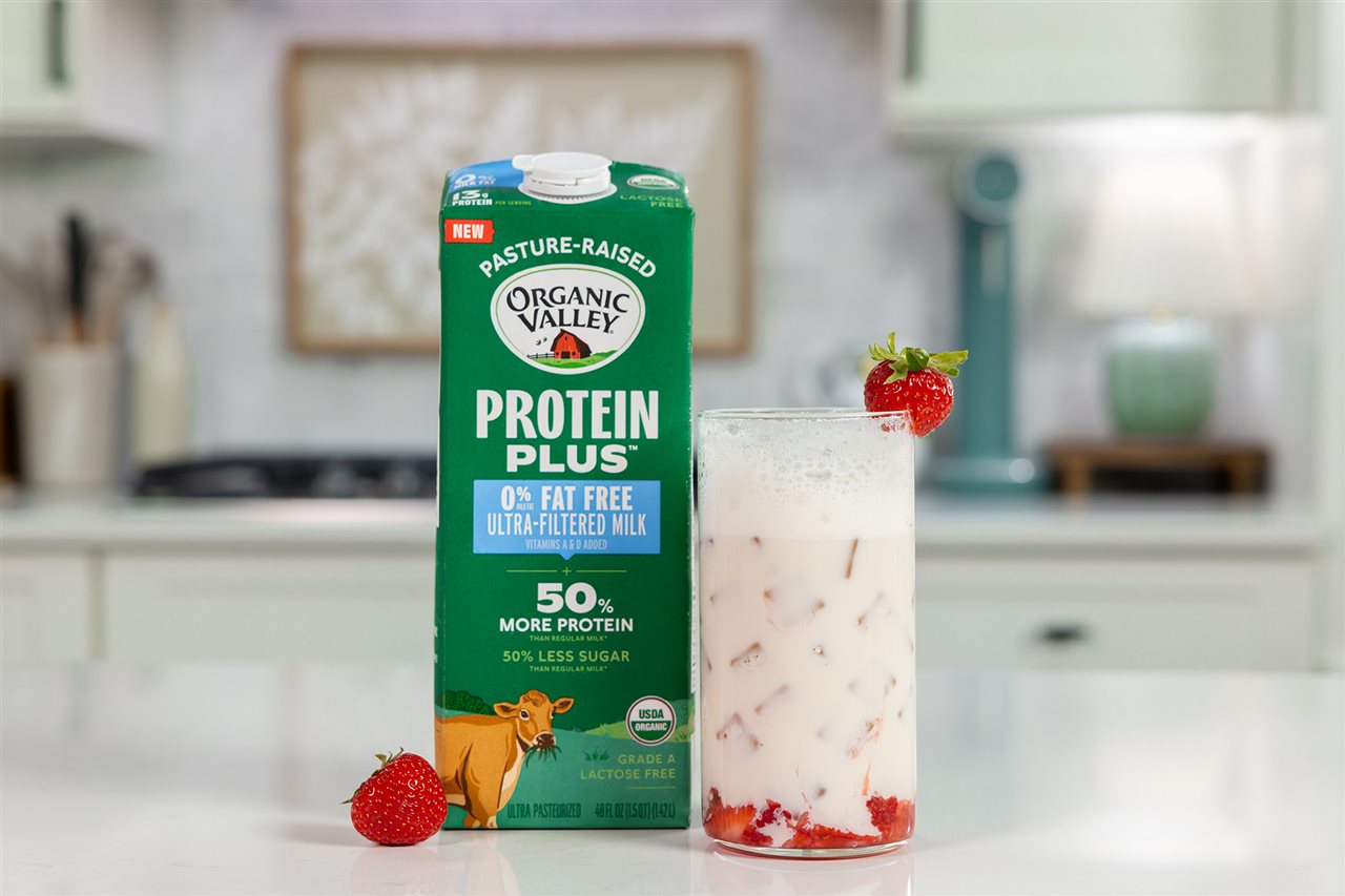A glass of Strawberry Shortcake Sparkling Milk next to a carton of Organic Valley Protein Plus Milk.
