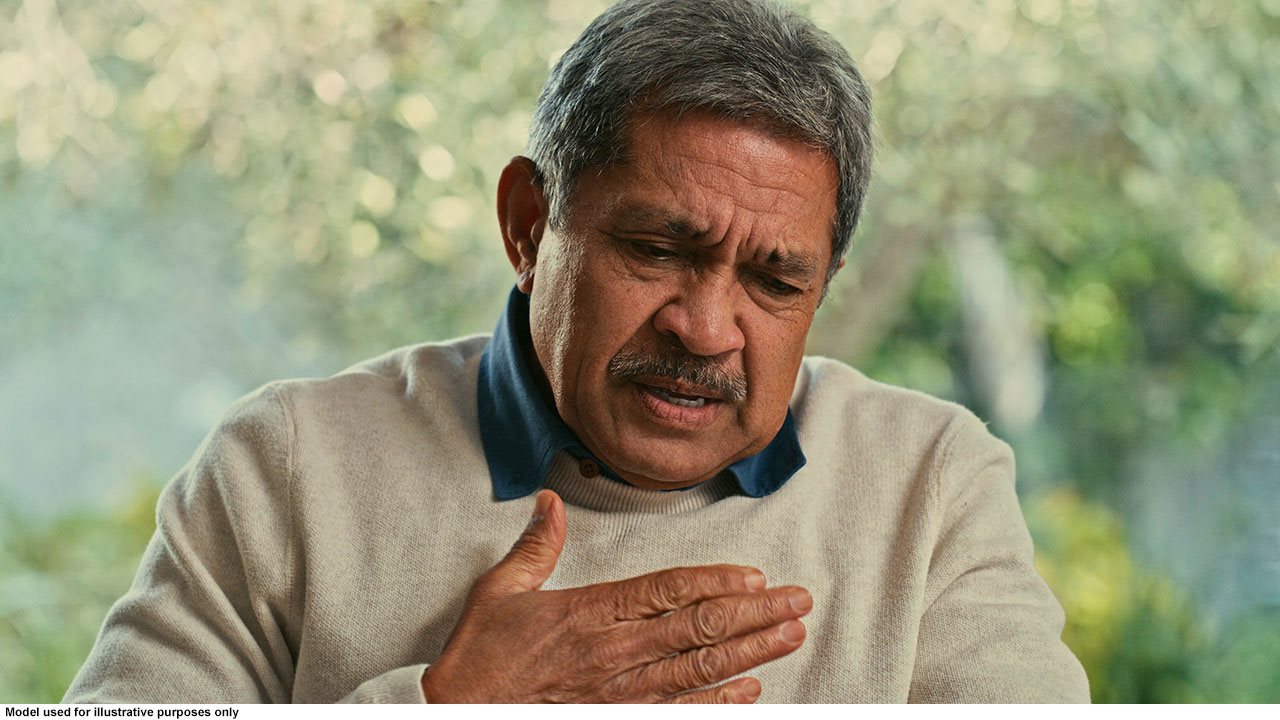 Older man in sweater holding his chest.