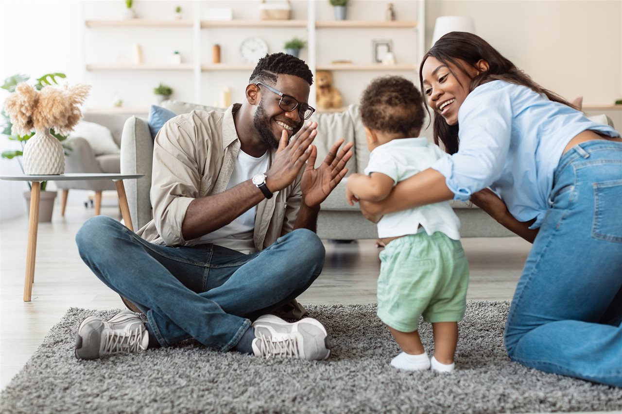 New parents happly encouraging their toddler to walk.