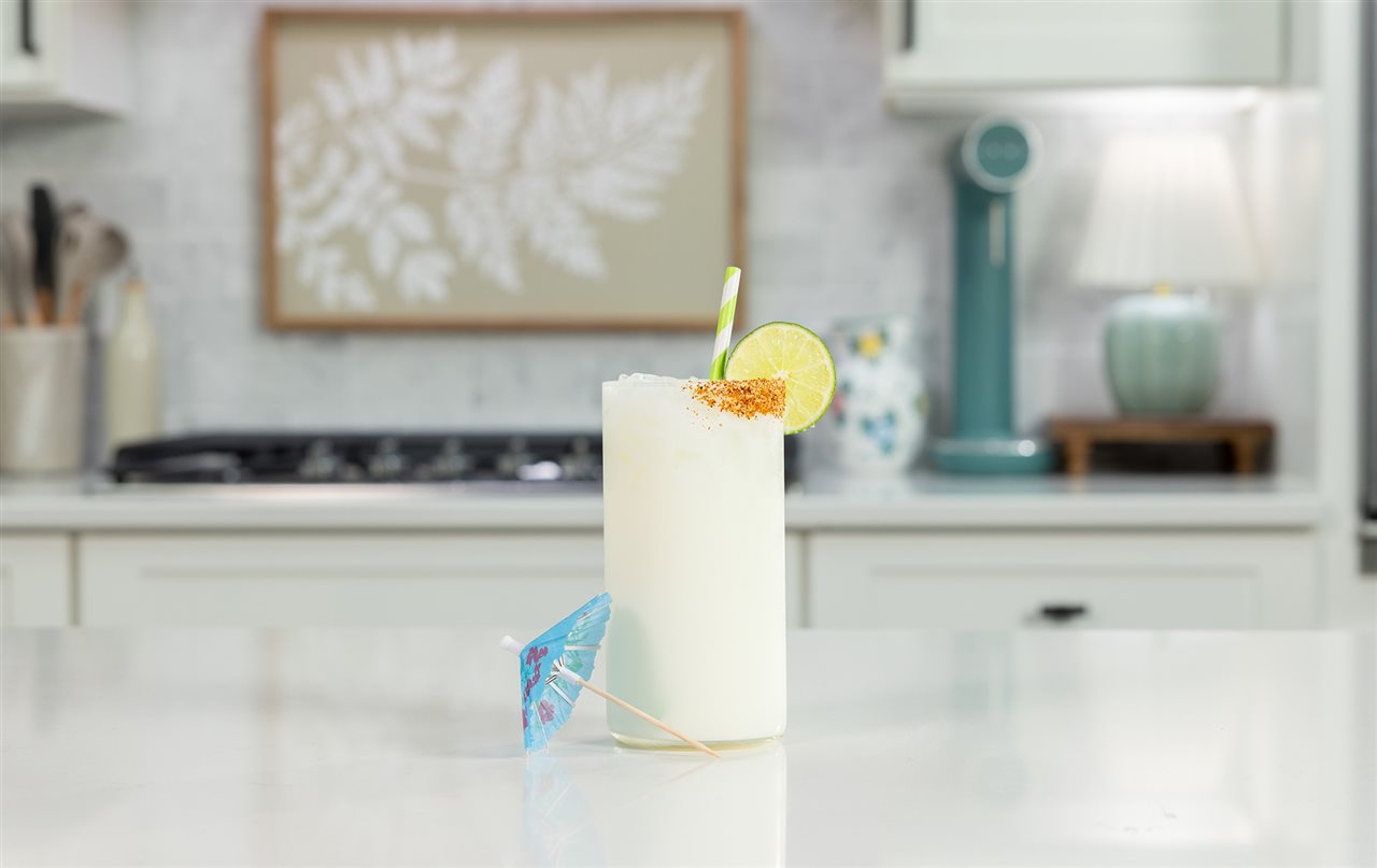 A glass of Organic Valley Coconut Lime Sparkling Milk with a slice of lime, a straw and a little paper umbrella.