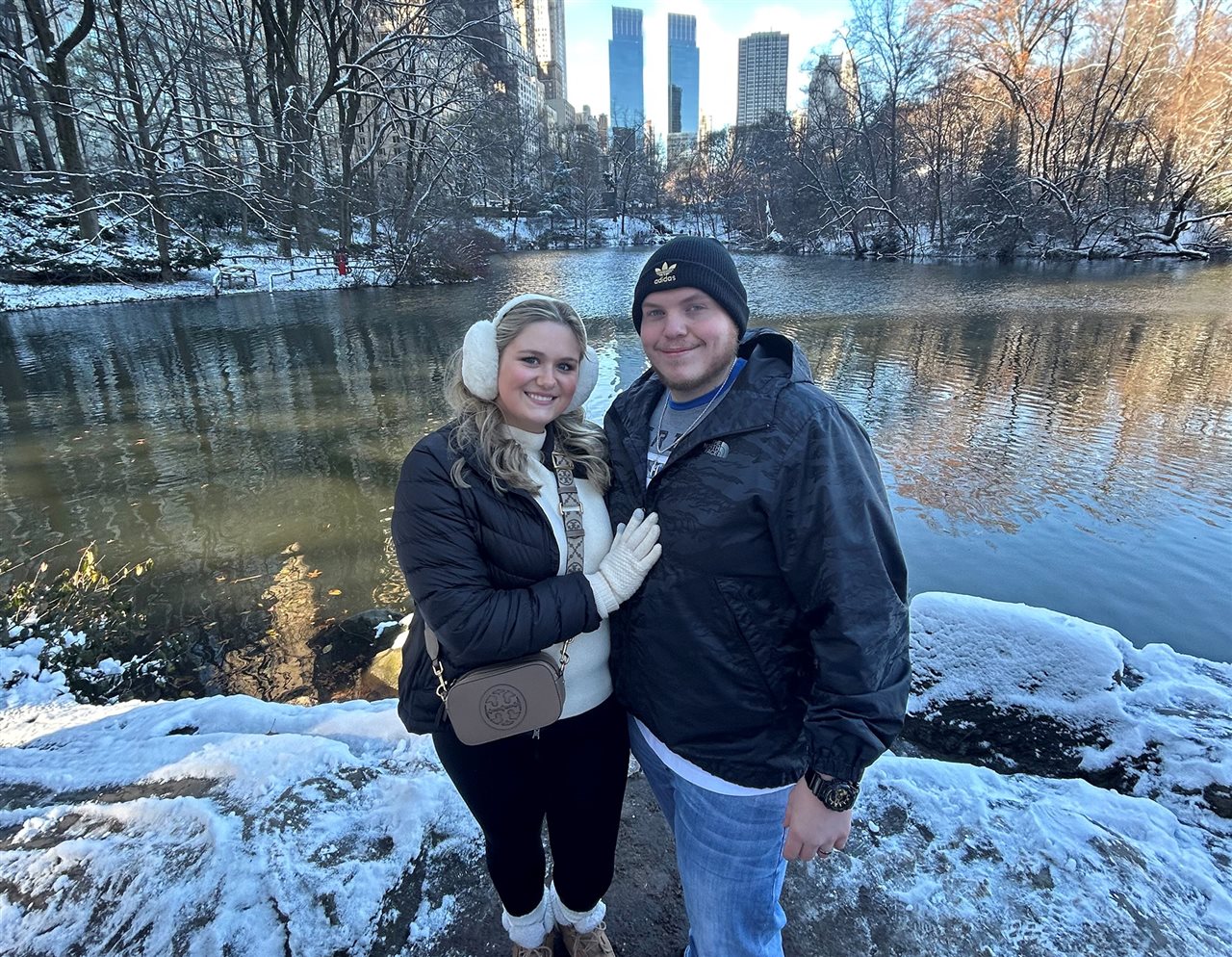 Sarah stands in front of a city pond in winter, next to her husband Chance.