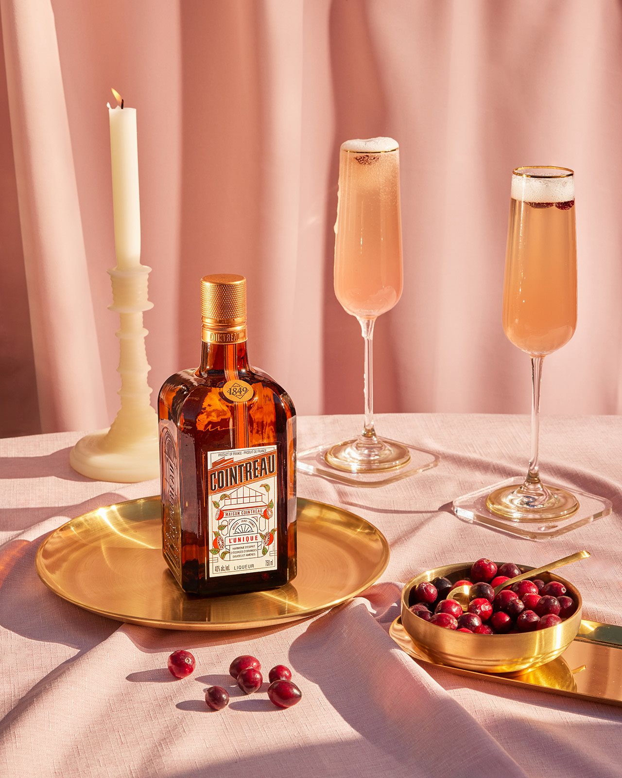 A bottle of Cointreau sits on a golden plate next to two stem glasses of Sparkling Cosmopolitans.