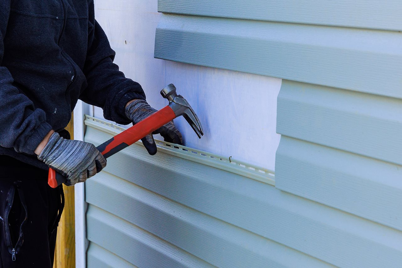 Man removing pieces of Vinyl siding from a home using a claw hammer.