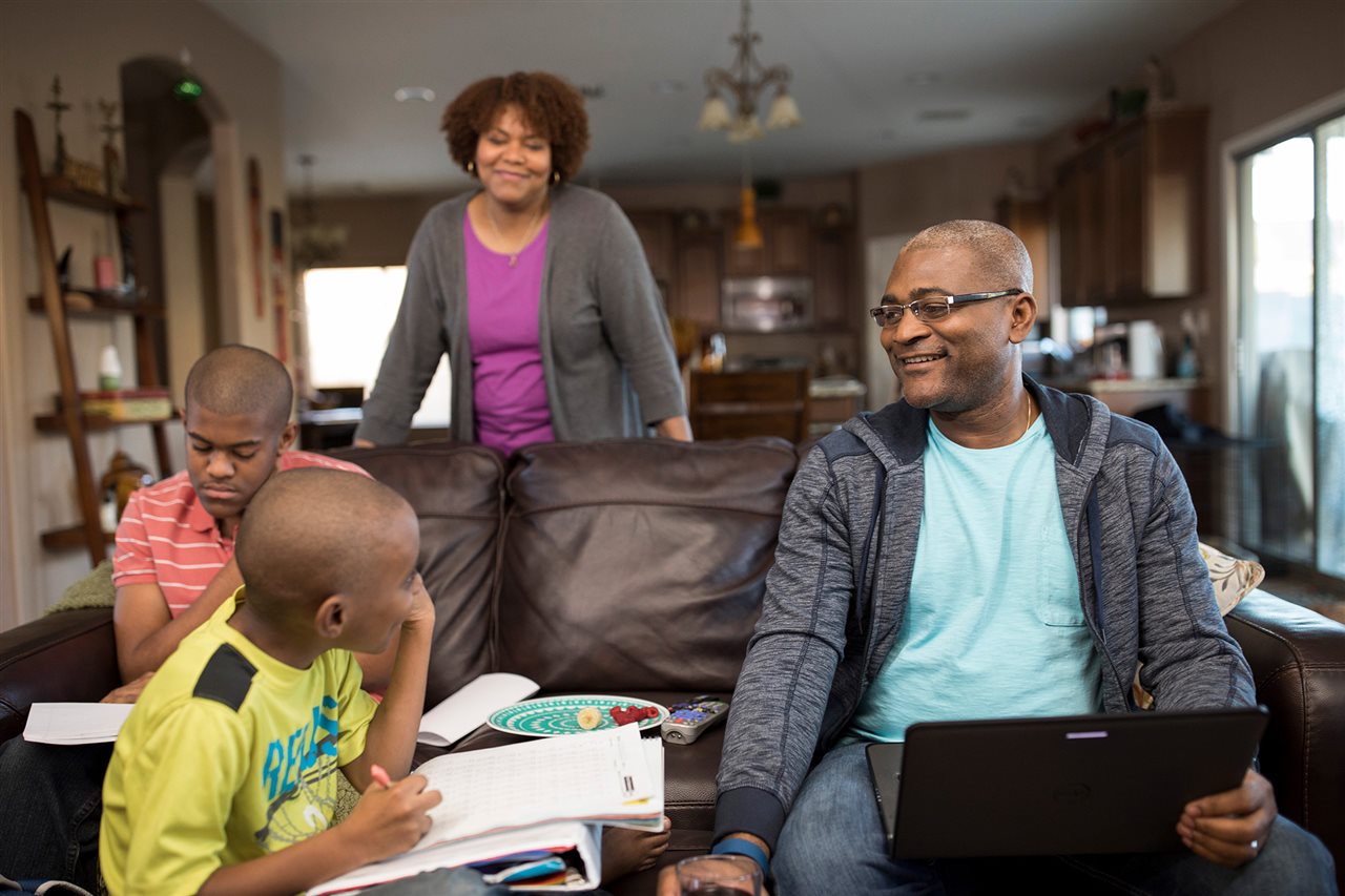 A family in the livingroom as dad works on laptop.University of Phoenix offers degree programs in 300 occupations,