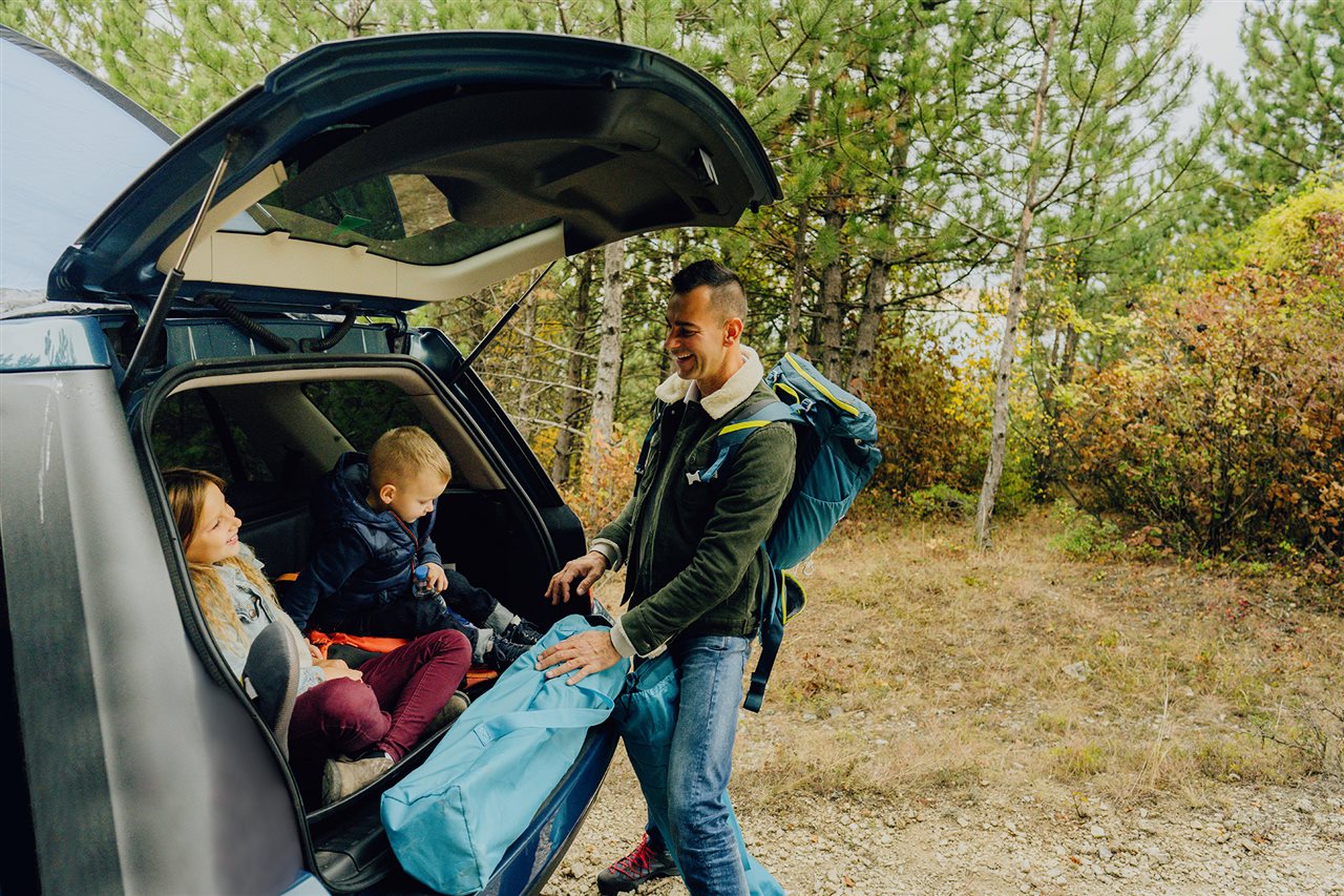 Dad talking with his son and daughter who are sitting in the back of his SUV while on a Fall outing.