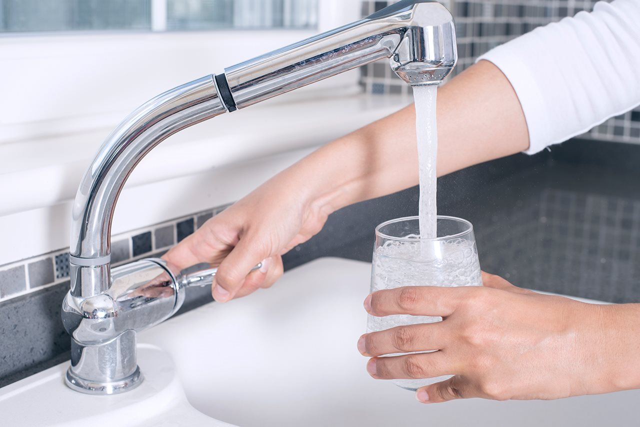 Woman filing up a glass with water from the kitchen faucet.