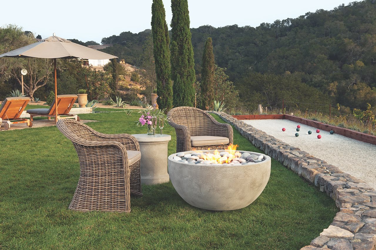 Two wicker chairs around a fire bowl next to an outdoor bocce ball court.