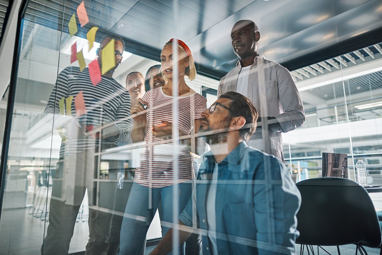 Group of co-workers working out systems with sticky notes on a glass wall.