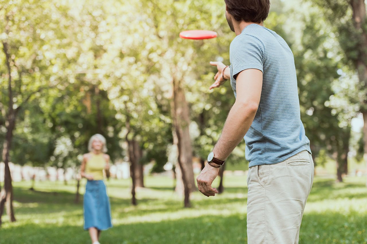 Man tossing a frisble to his girlfriend in a park