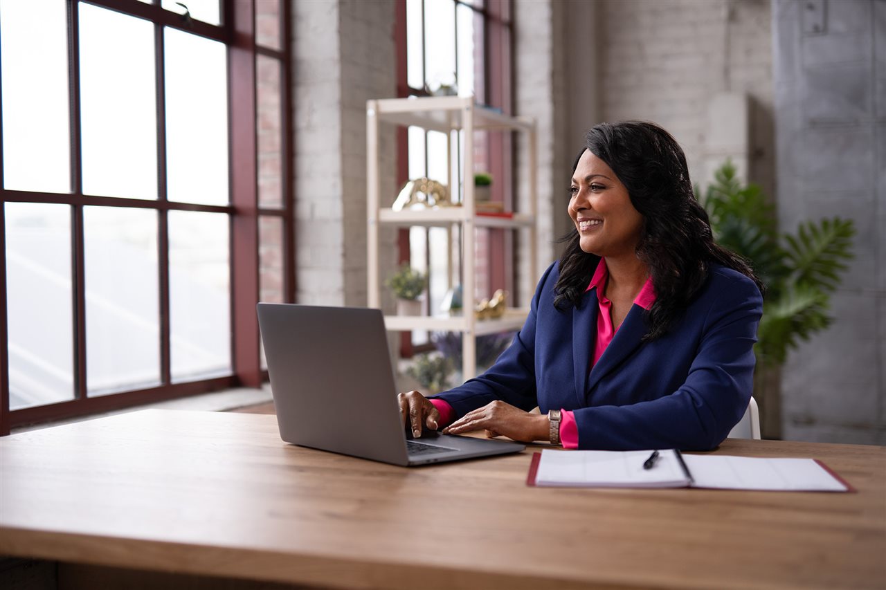 A woman smiles as she sits in her office, studying on her laptop.