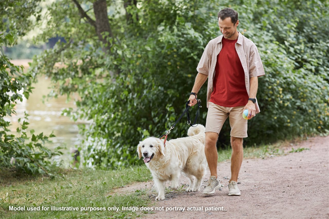 Adult man wearing casual clothing walking his dog on a sunny day.