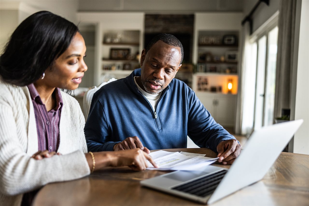 Couple sitting at their kitchen table using a laptop to source options for medication.