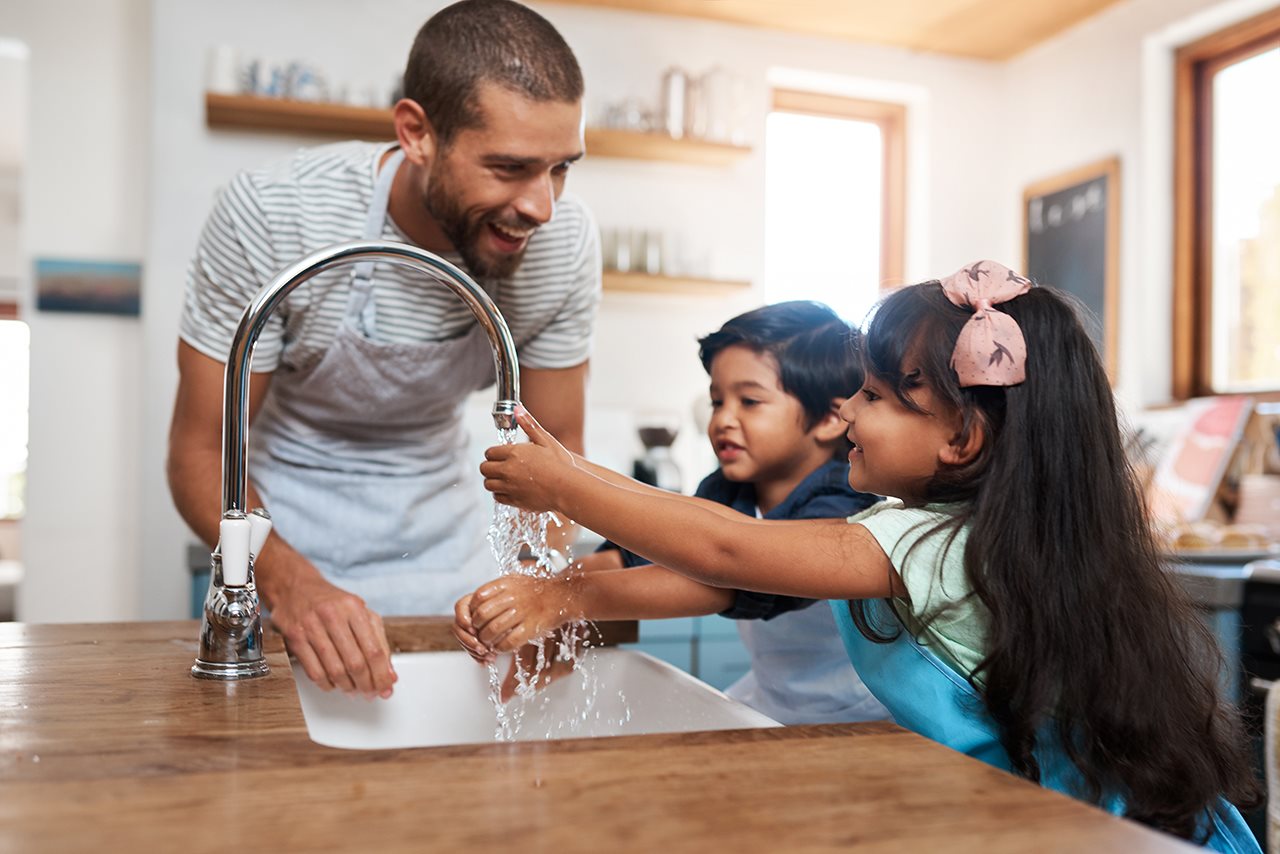 Dad asisting his children to wash their hands in the kitchen sink
