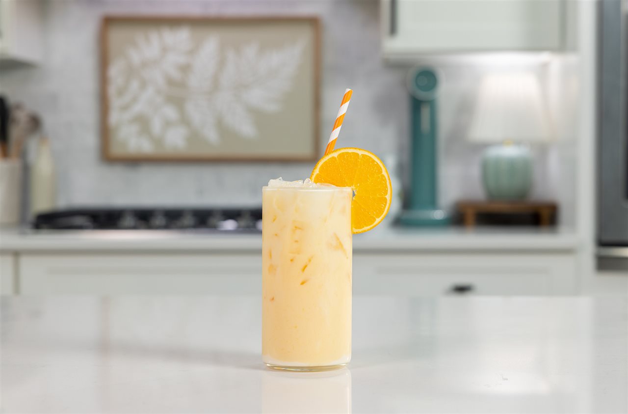 Organic Valley Sparkling Orange Cow Milk in a glass with a slice of orange and a straw.
