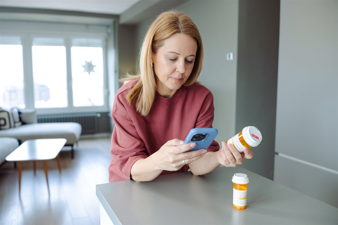 Woman at home looking at precription bottle and calling the pharmacy. BioPlusRX is a specialized, personal pharmacy.