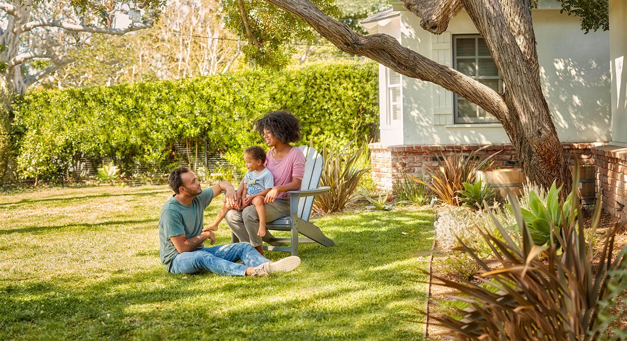 A mother, father, and their child sit and relax in the front yard of their home.