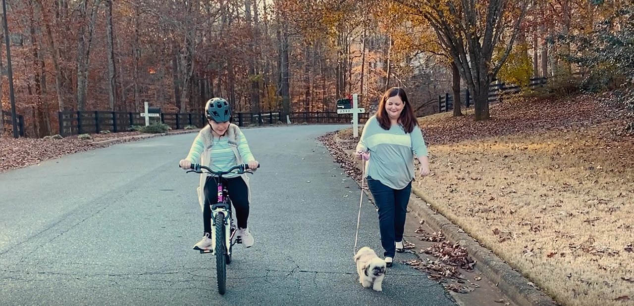 Alison outside on a Fall day, walking her dog while a child rides a bike next to her.