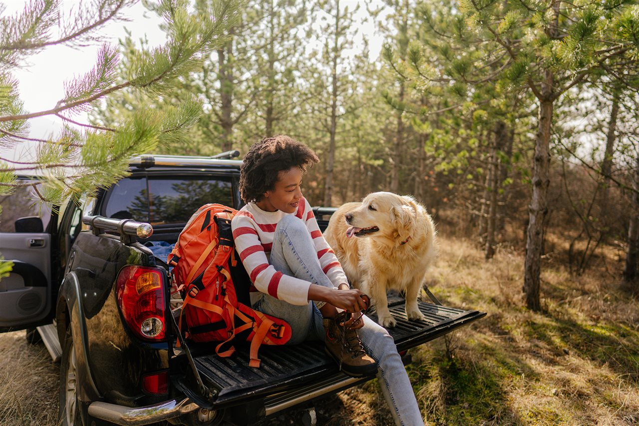 Woman tying her boots as she sits on the tailgate of her truck with her golden retriever.