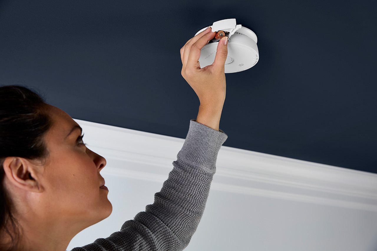 A woman removes a battery from her smoke alarm.