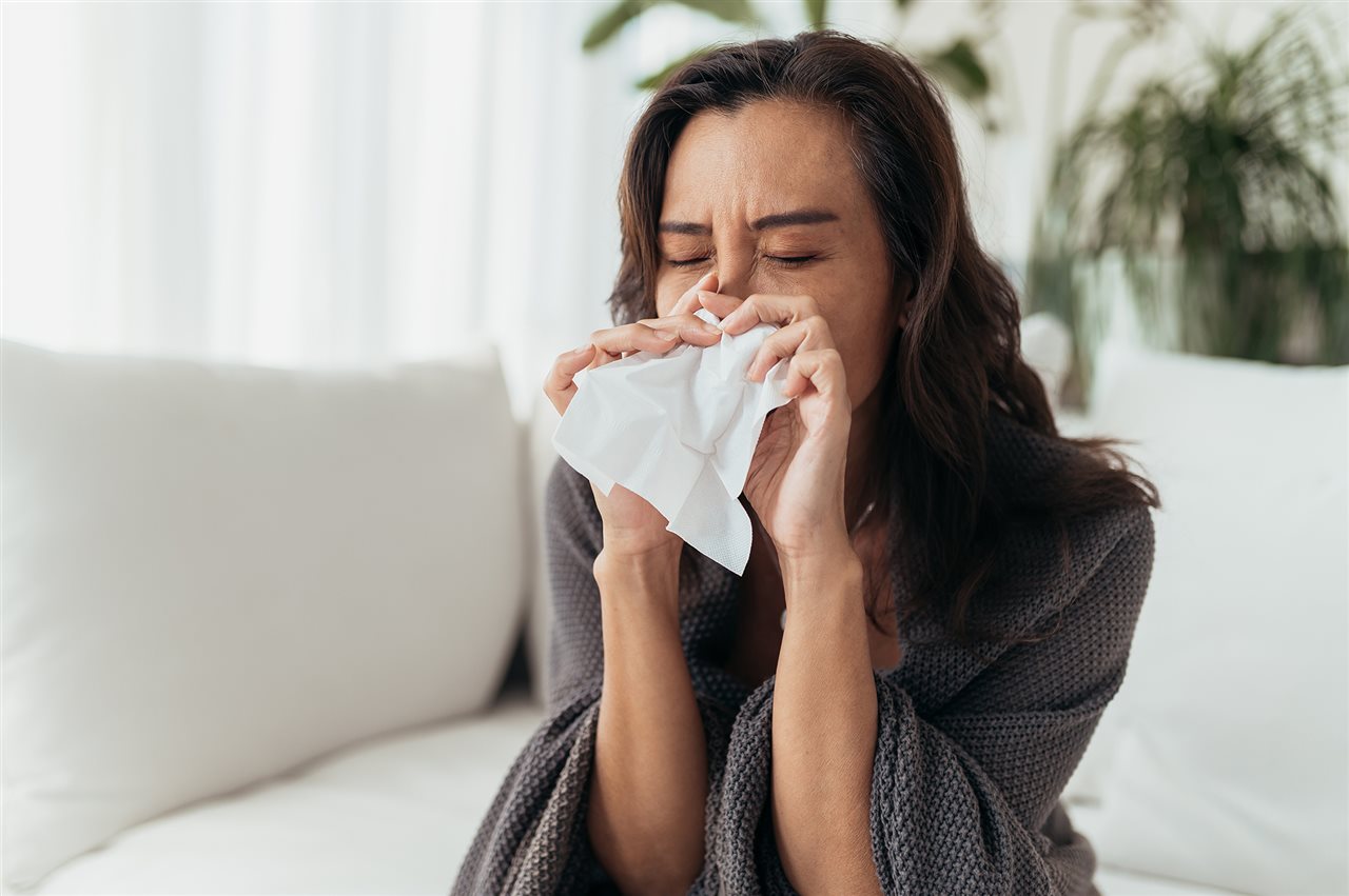 Una mujer al&eacute;rgica se sienta en un sof&aacute; con un pa&ntilde;uelo de papel. Los sistemas de calefacci&oacute;n y refrigeraci&oacute;n central Lennox mejoran la calidad del aire.