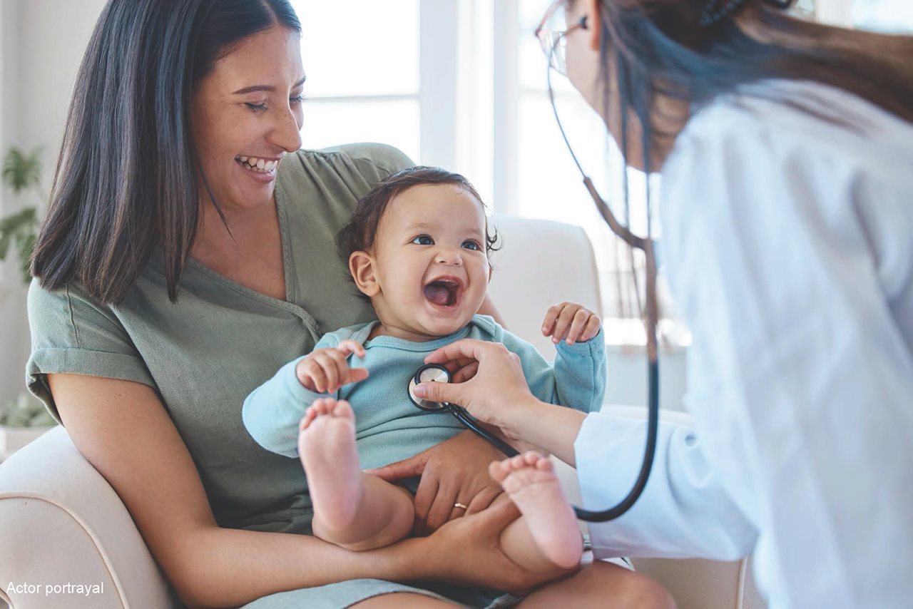 Woman holding a baby while doctor listens to baby's heart with a stethoscope.