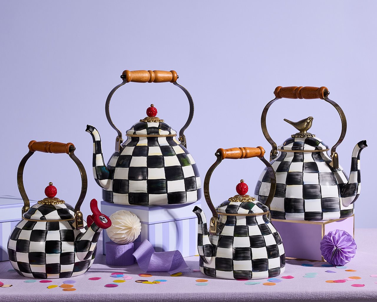 Four checkered MacKenzie-Childs tea kettles against a purple backdrop