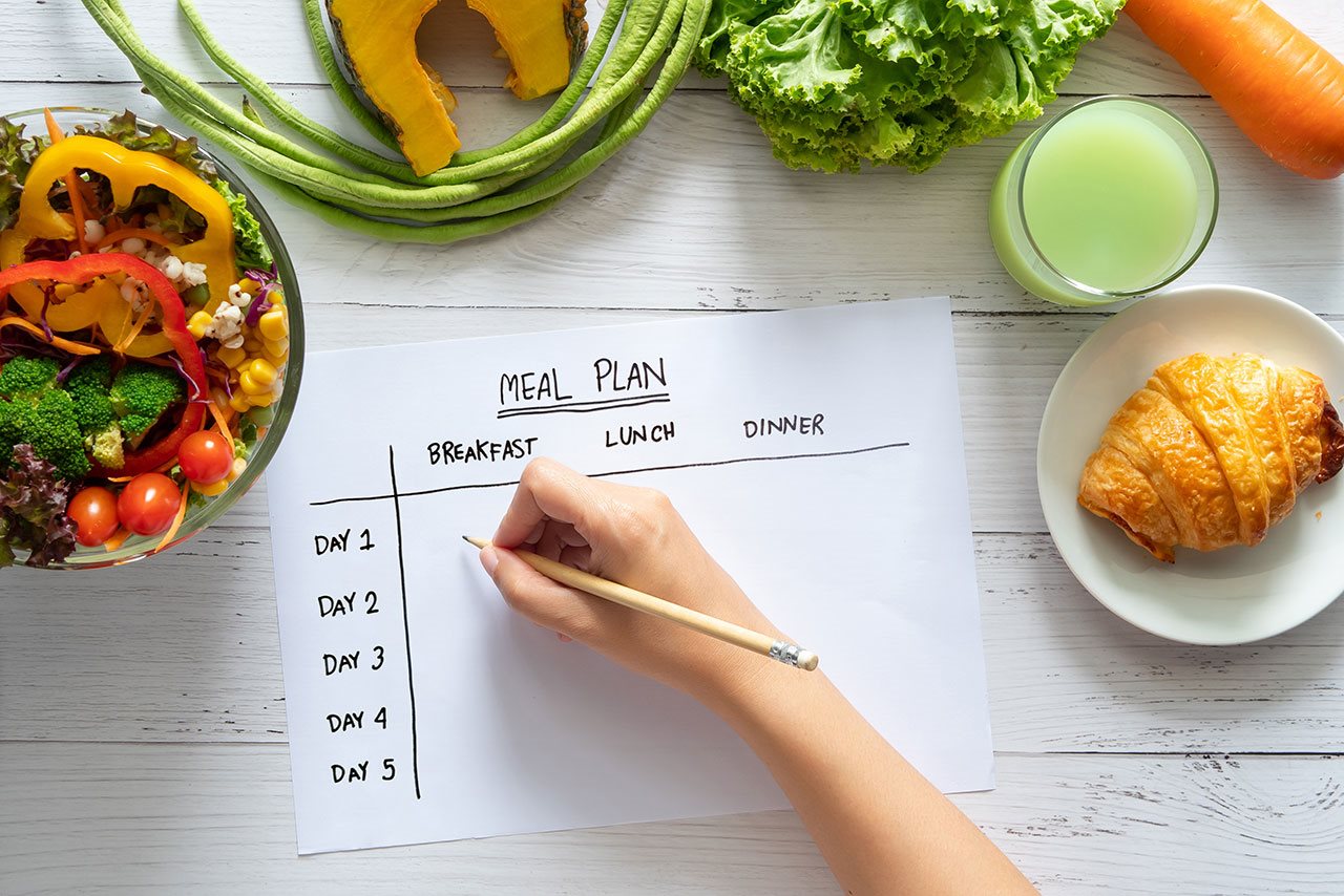 Menu planning spread sheet with bowls of vegetables on a table