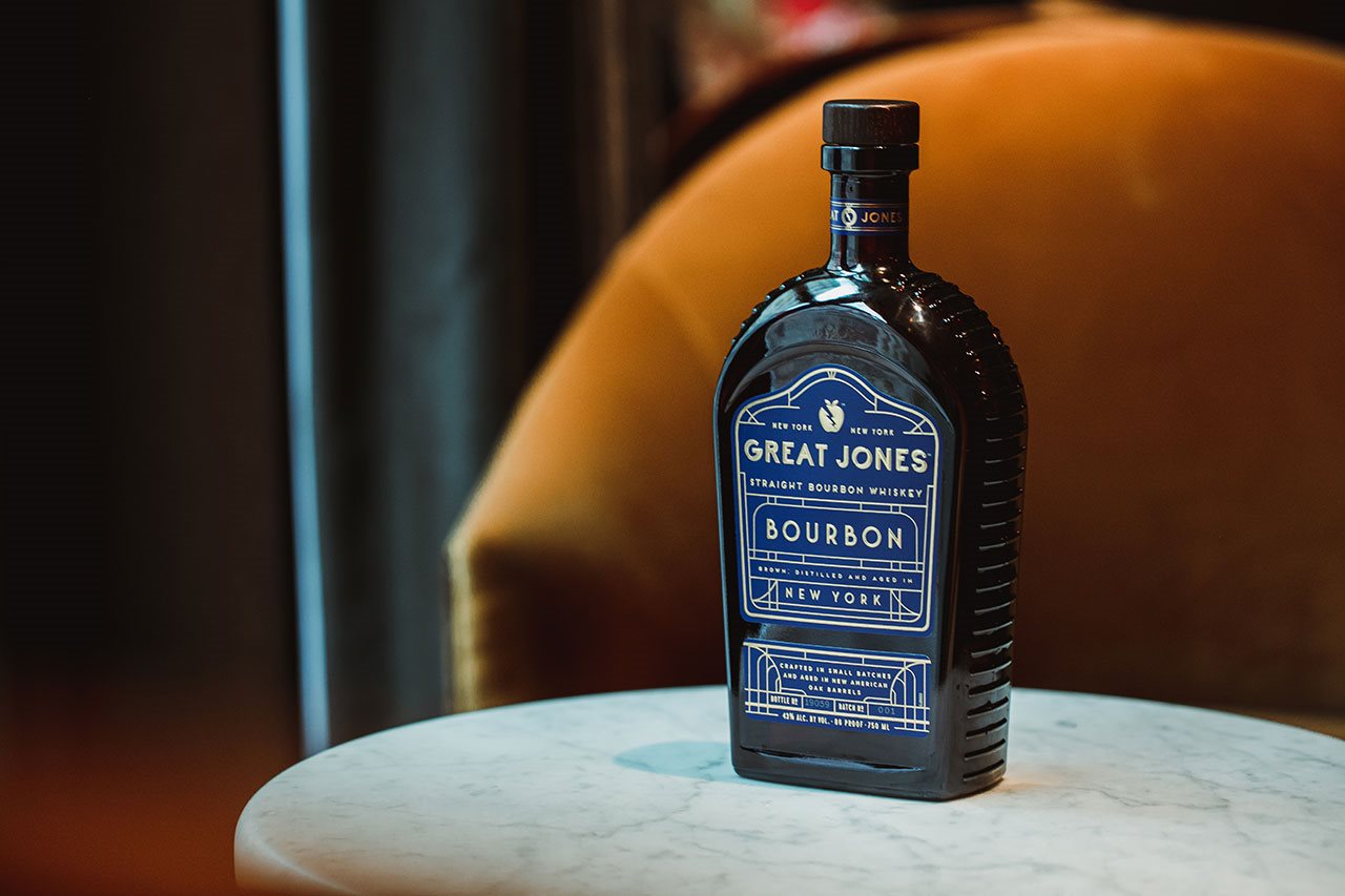 A bottle of Great Jones Bourbon, on a marble table next to a couch.