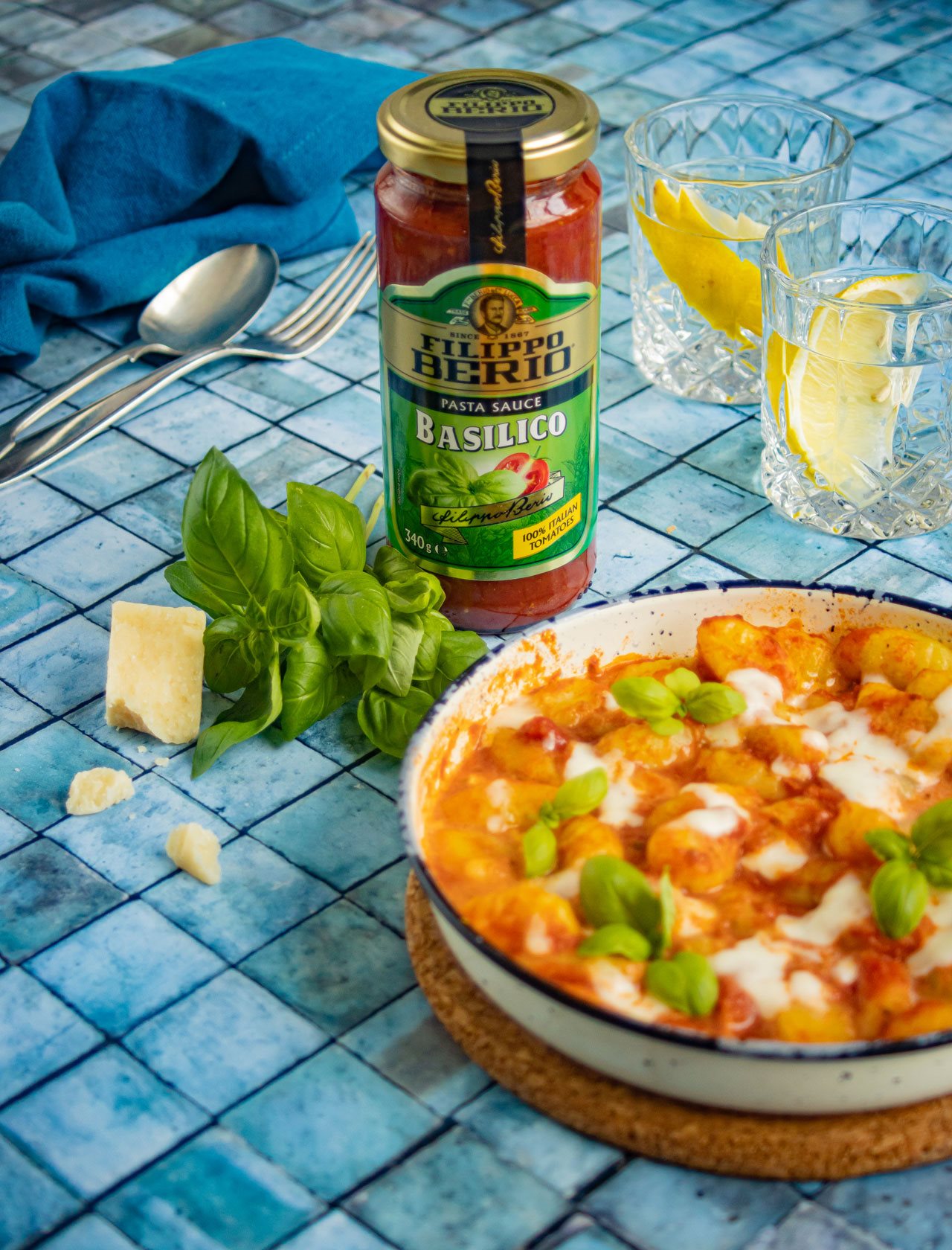A bowl of gnocchi and tomato basil and a jar of Filippo Berio Basilico on a tiled counter top.