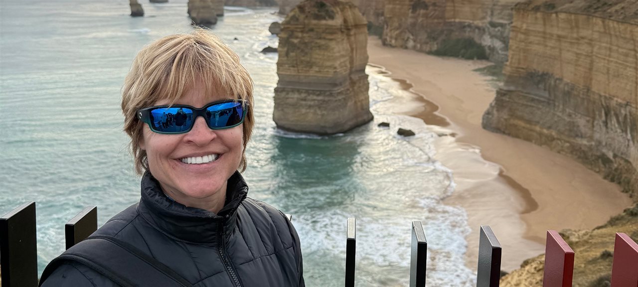 Sherry wearing sunglasses, smiling on a beach.