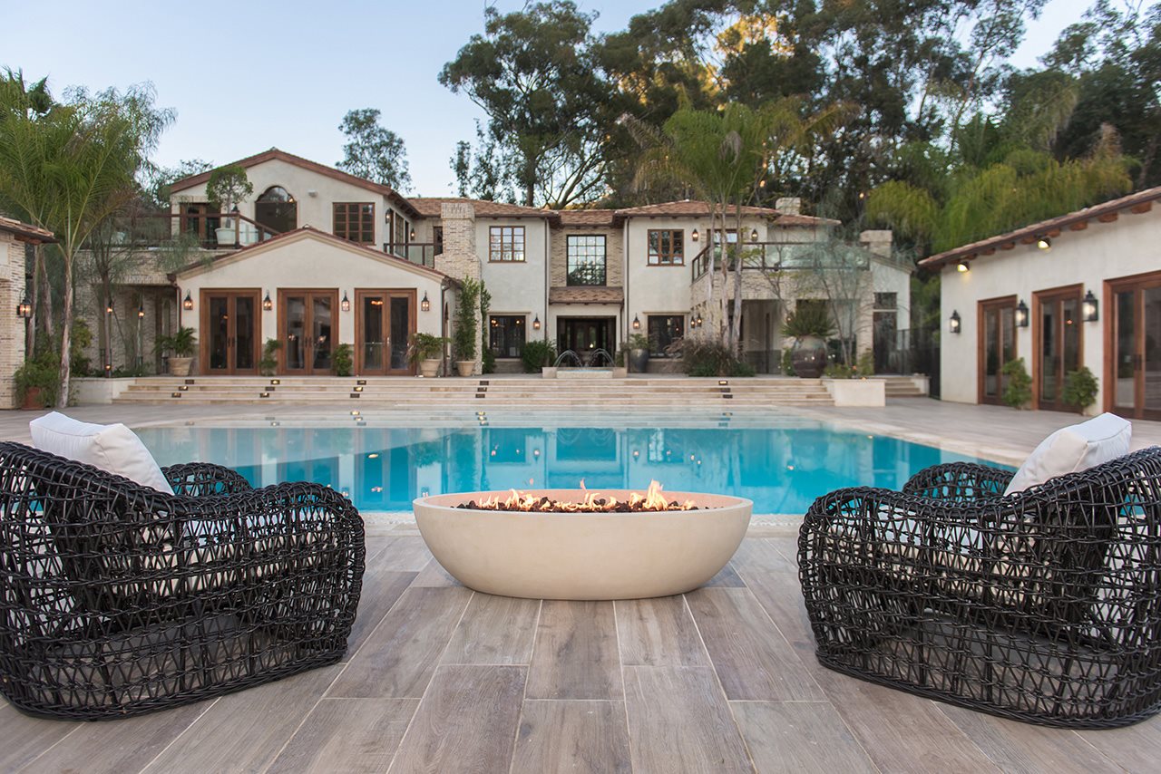 A fire bowl next to two chairs in front of a pool.