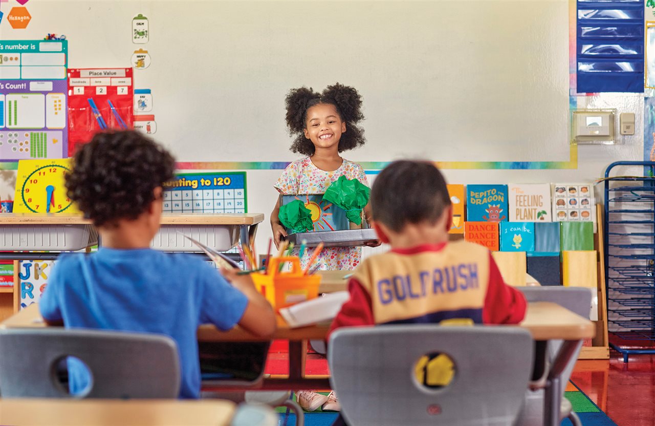 A little girl at school presents a diorama of trees she made in front of her class.
