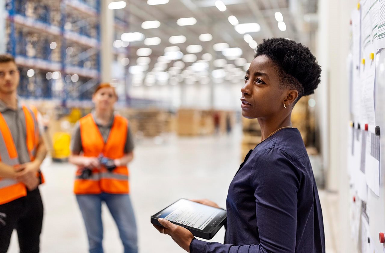 A woman with a tablet briefs warehouse workers