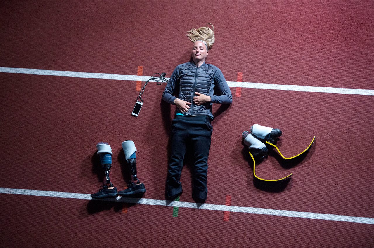 Athletic woman laying down with prothetic legs next to her. Embla designs and manufactures high-performance prosthetics.