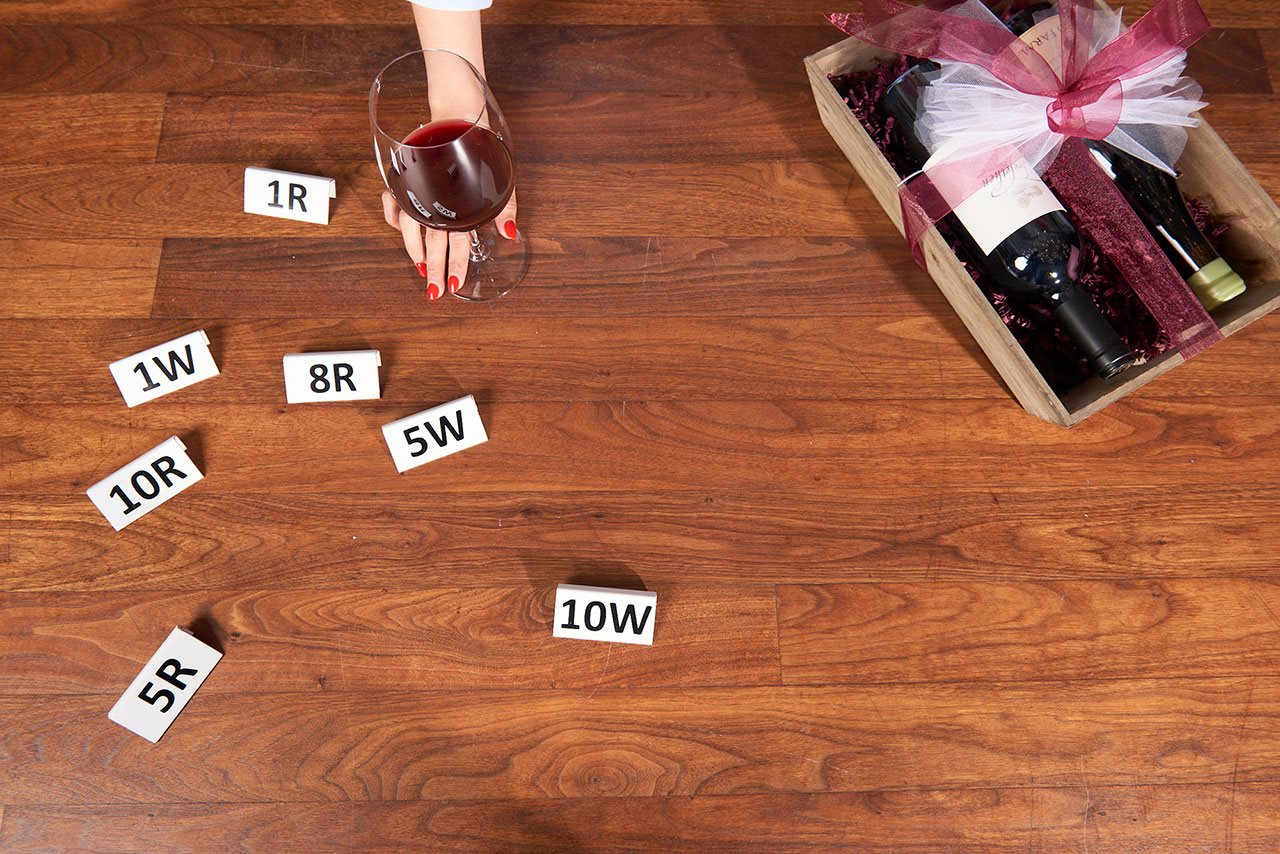 Person holding a glass of wine with gift box and markers on a table