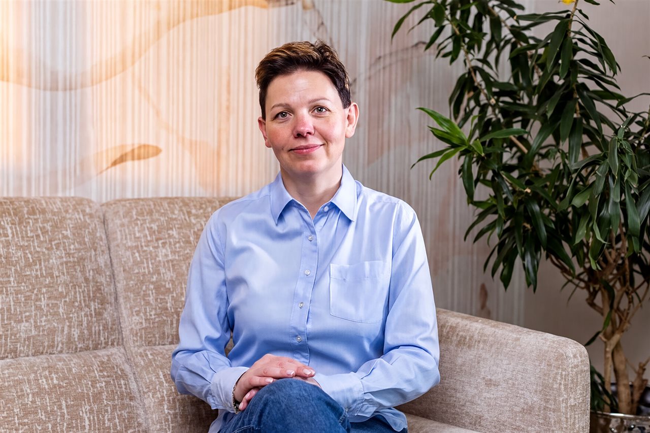 Smiling Ewa, living with Primary Immunodeficiency (PI), sitting on a couch.