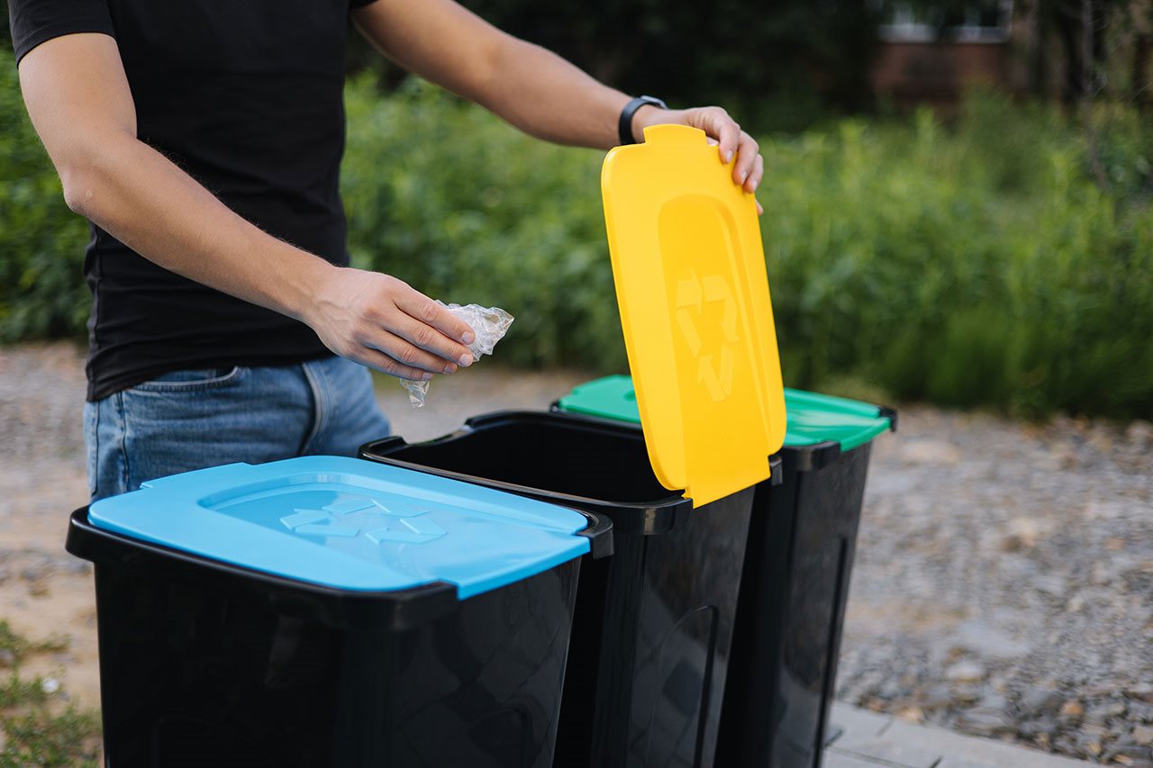 Young man recyling a plastic bag in a park recyling bin