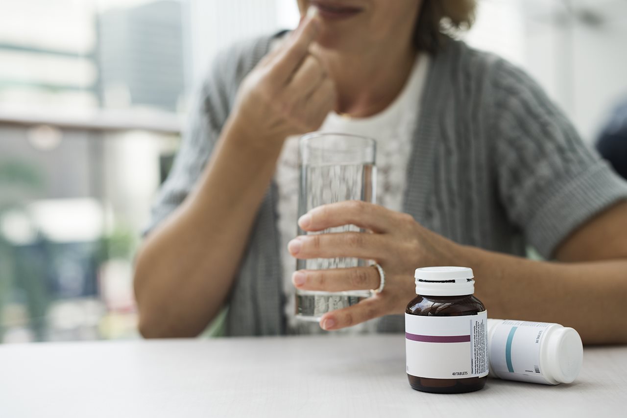 woman wearing a gray sweater taking a pill with a glass of water