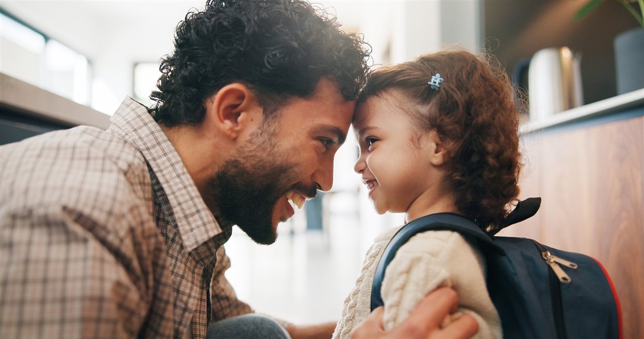 Dad and little daughter with her backpack hugging in the kitchen.