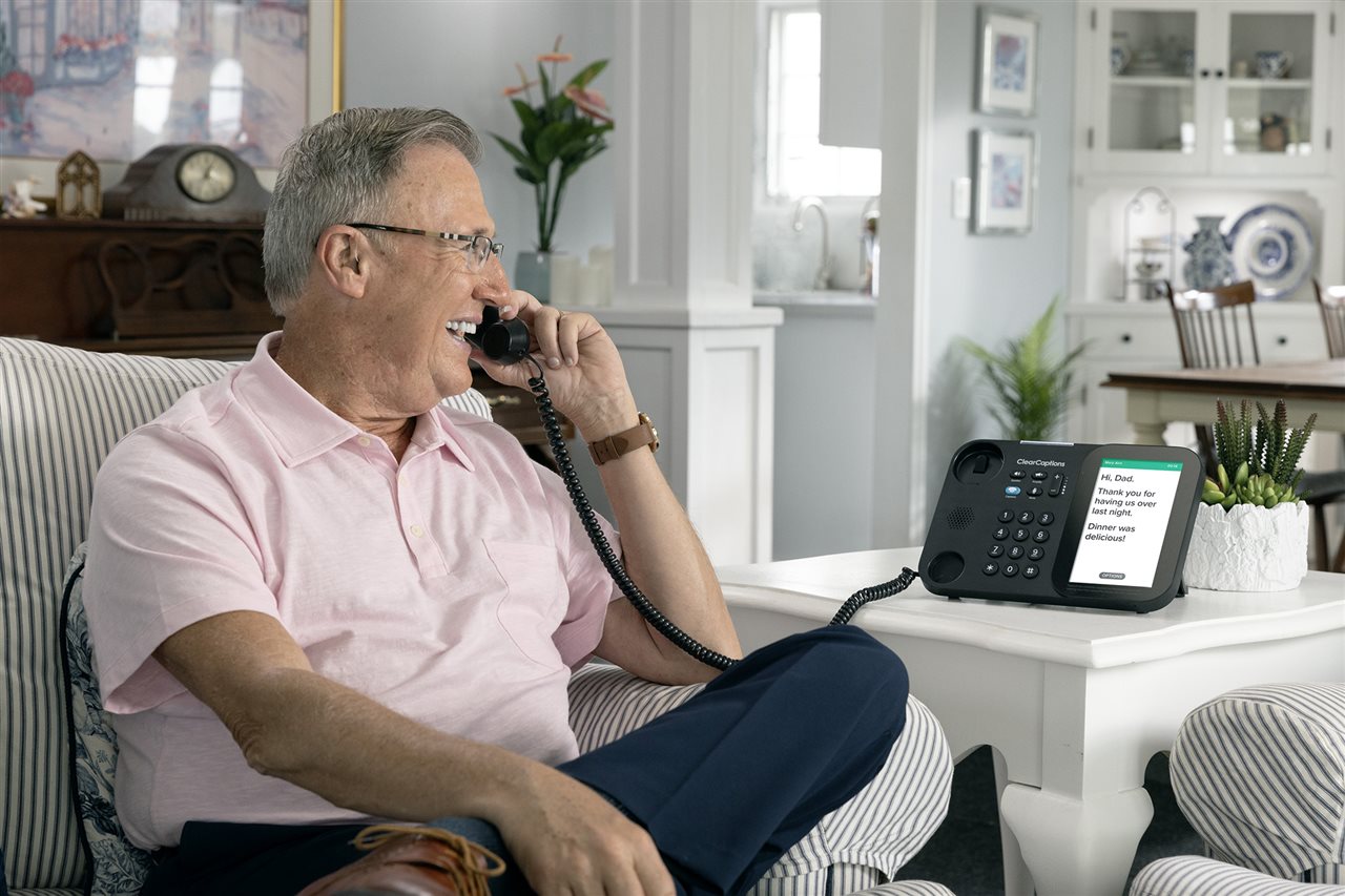 Senior man on the couch talking with his son using a ClearCaptions phone.